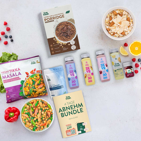 LiveFresh Abnehmbundle mit Vegan Tikka Masala. Schoko Porridge. Slim Support. Protein Drinks. Shots und dem Guide "4 Tage Abnehm Bundle" auf hellem Untergrund neben buntem Obst und zubereiteten Mahlzeiten.