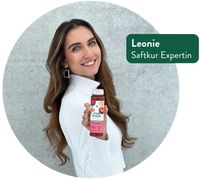 Junge Frau mit langen braunen Haaren hält einen LiveFresh Saft in der Hand und lächelt; eingeblendeter weißer Text auf grünem Hintergrund: „Leonie – Saftkur Expertin“