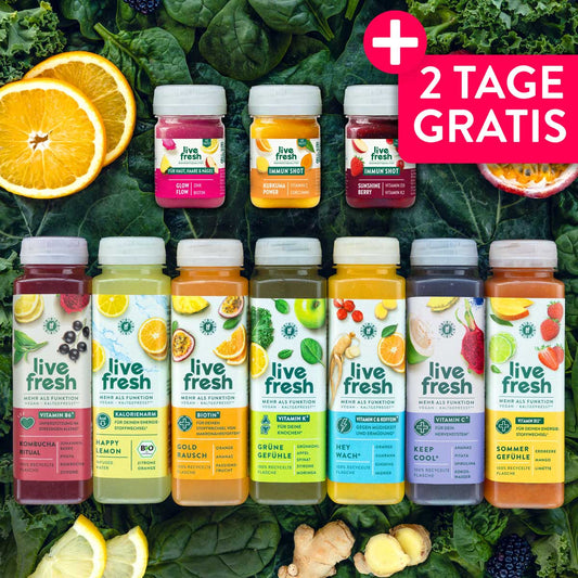 Sieben bunte LiveFresh Säfte und drei Shots für eine Saftkur auf einem Bett aus grünem Blattgemüse mit frischen Früchten und Ingwer. Pinker Aktionshinweis mit der Aufschrift "2 TAGE GRATIS".