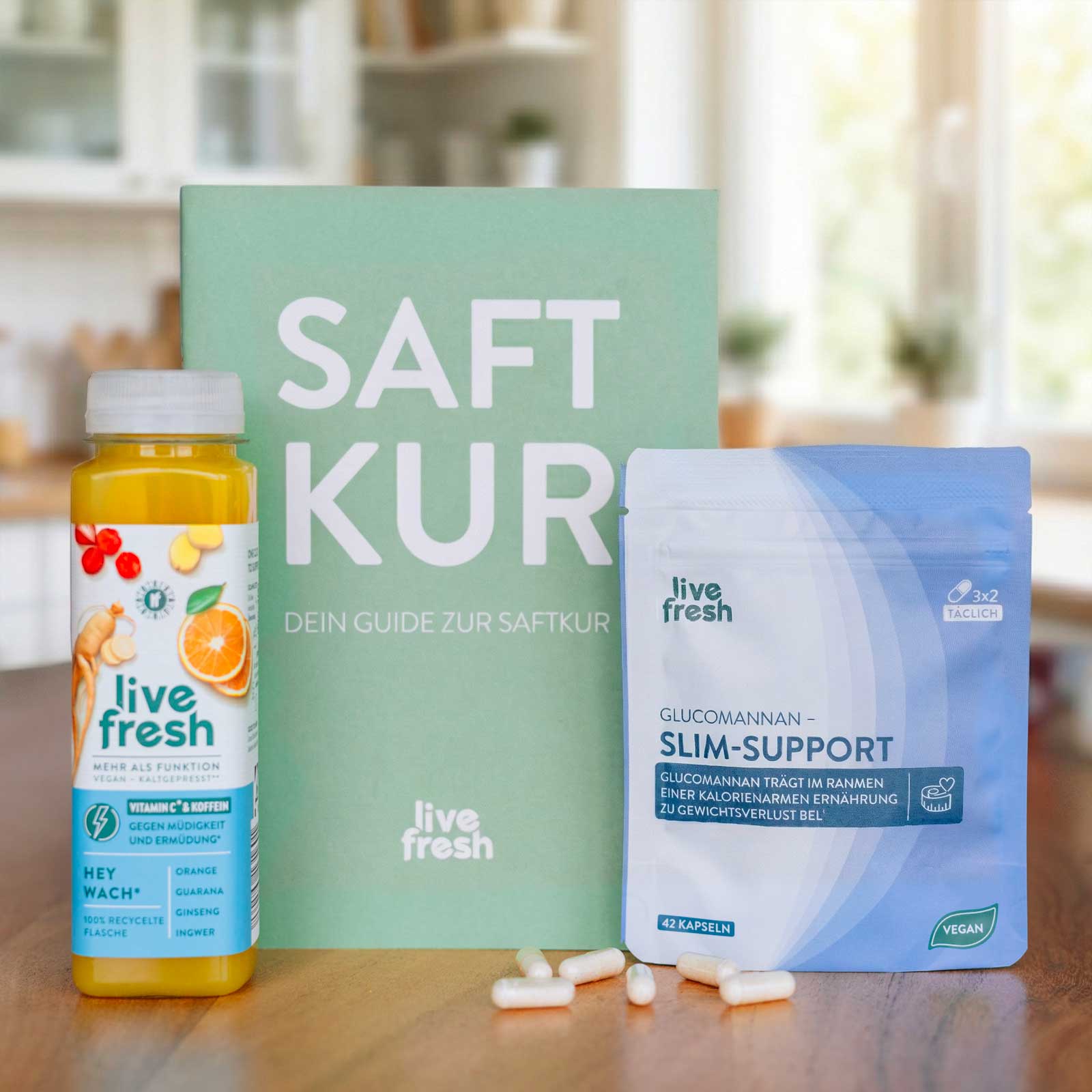Produktset mit einer Flasche „live fresh“ Saft, einem Buch mit dem Titel „SAFT KUR“ und einem Beutel „Glucomannan Slim-Support“ steht auf einem Tisch, davor liegen mehrere Kapseln. Auf der Verpackung ist der Text „GLUCOMANNAN – SLIM-SUPPORT“ sowie „GLUCOMANNAN TRÄGT IM RAHMEN EINER KALORIENARMEN ERNÄHRUNG ZU GEWICHTSVERLUST BEI“ gut sichtbar.