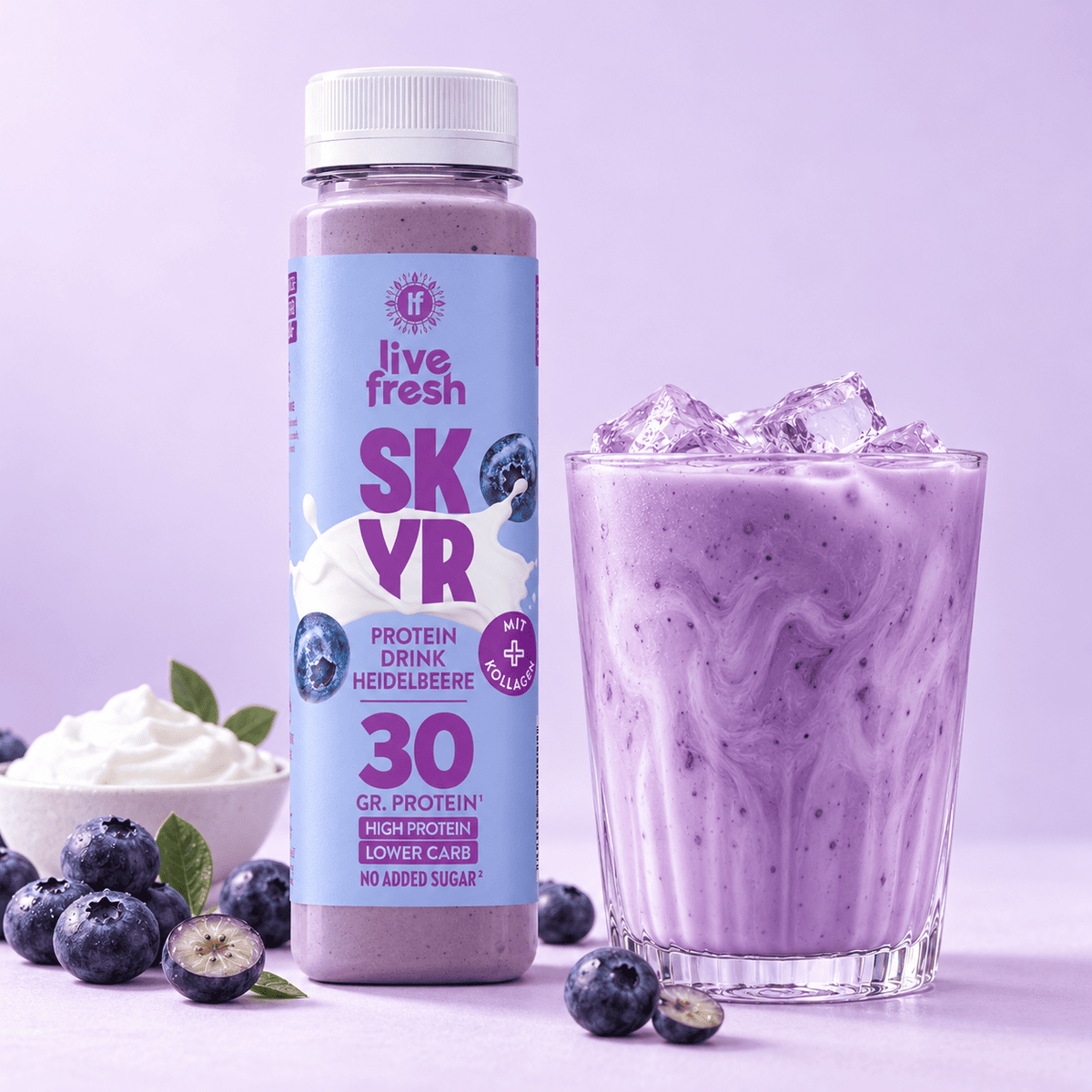 Live Fresh Skyr Protein Drink Heidelbeere neben einem Glas mit eisgekühltem cremigem Heidelbeerdrink. Auf der Verpackung steht "live fresh SKYR PROTEIN DRINK HEIDELBEERE MIT KOLLAGEN 30 GR. PROTEIN HIGH PROTEIN LOWER CARB NO ADDED SUGAR". Frische Heidelbeeren und eine Schale mit cremigem Skyr stehen daneben.