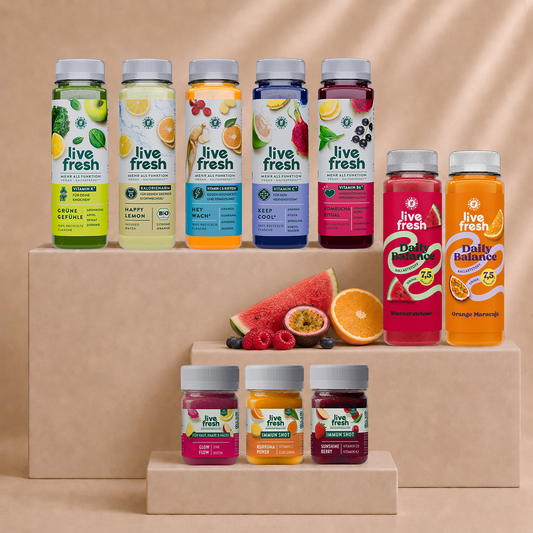 Live Fresh Balance Kur mit verschiedenen Säften und Shots auf beigen Podesten. Zu sehen sind unter anderem Grüne Gefühle, Happy Lemon, Hey Wach, Keep Cool, Kombucha Ritual sowie Daily Balance Drinks und Immun Shots mit frischem Obst.