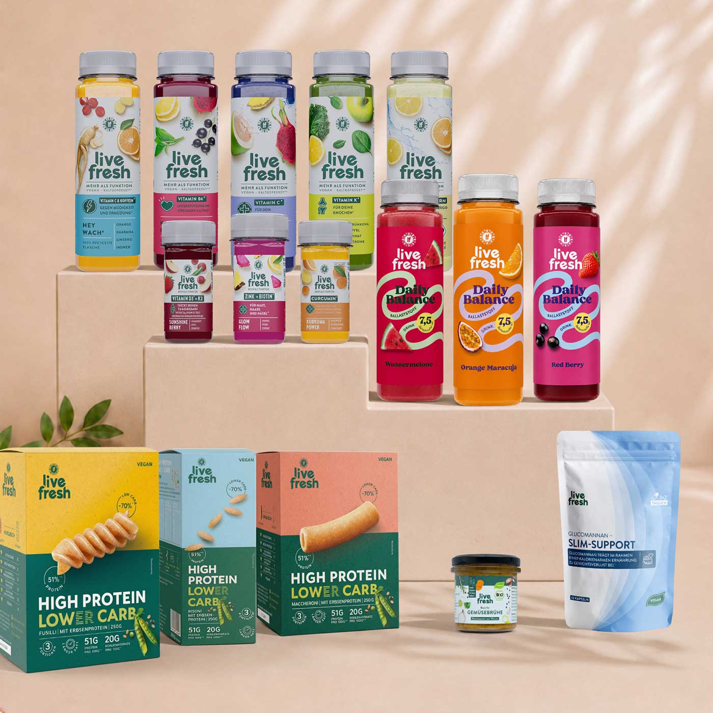 Eine Auswahl an LiveFresh-Produkten ist auf beigefarbenen Podesten dekorativ präsentiert. Das Sortiment umfasst Saftflaschen, Functional Shots, Ballaststoffgetränke, High-Protein-Lower-Carb-Produkte, Gemüsebrühe und ein Glucomannan-Pulver vor einem hellen Hintergrund mit dezenten Licht- und Schatteneffekten.