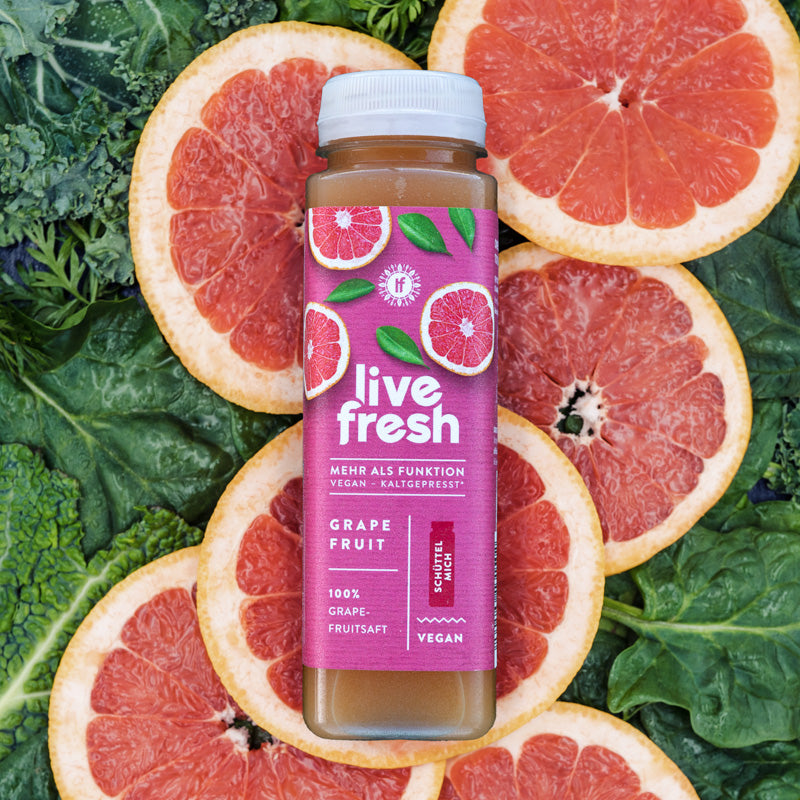 Das Bild zeigt eine Flasche "Live Fresh" Saft, die vor einem Hintergrund aus frischen Grapefruitscheiben und Grünkohl liegt. Der Saft mit dem Geschmack "Grapefruit" ist zu 100 % vegan und kaltgepresst. Auf dem Etikett steht „Mehr als Funktion“ und „Schüttel mich!“, was darauf hinweist, dass der Saft vor dem Verzehr geschüttelt werden sollte.