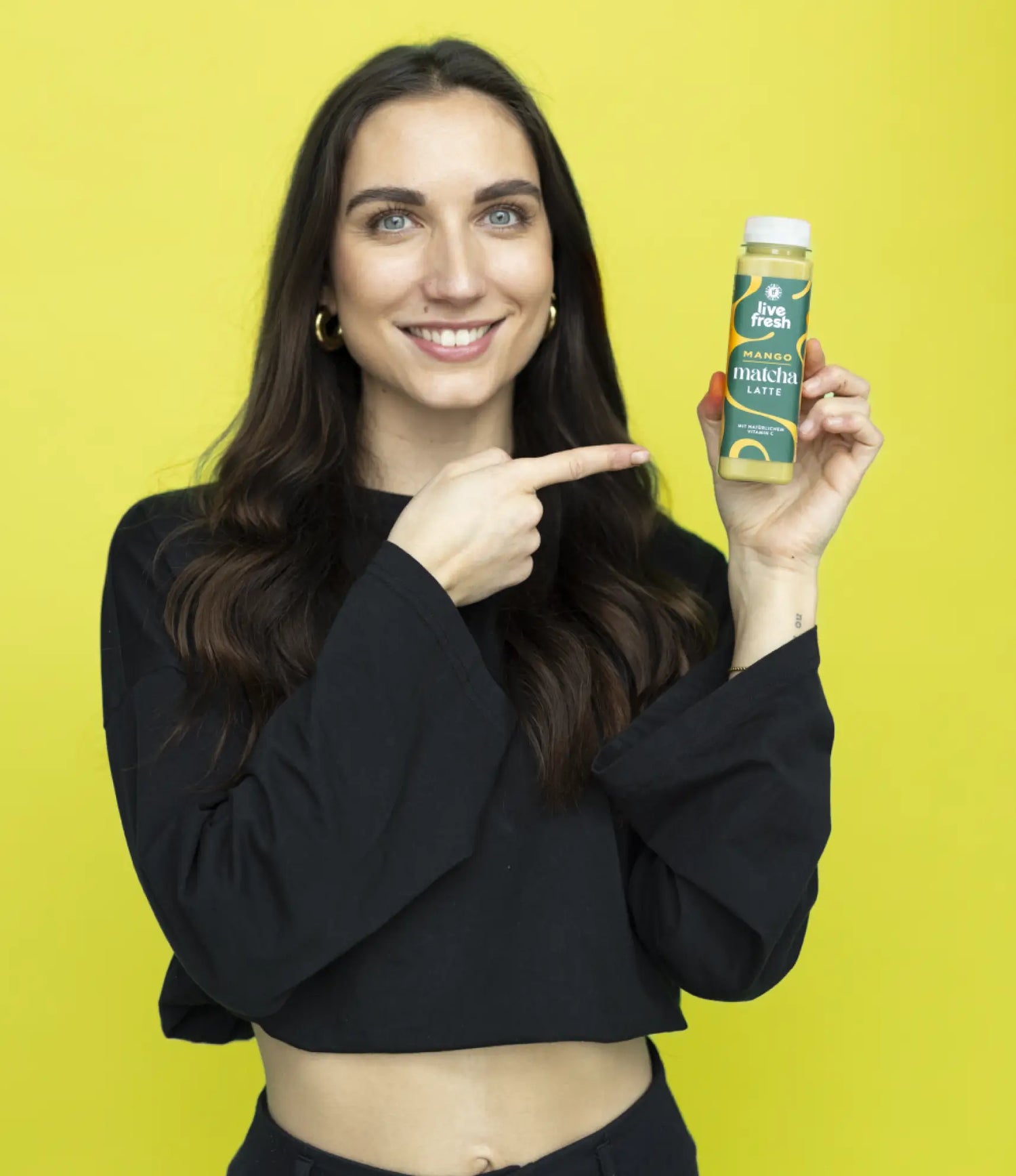 Person smiling while presenting LiveFresh mango matcha latte in a small bottled drink. The product is centered and easy to identify.
