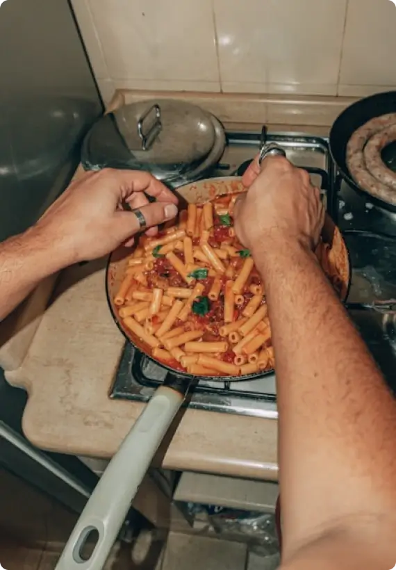 Hände garnieren frische Kräuter auf eine Pasta in Tomatensoße in einer Pfanne auf dem Herd während sie frisch gekocht wird.