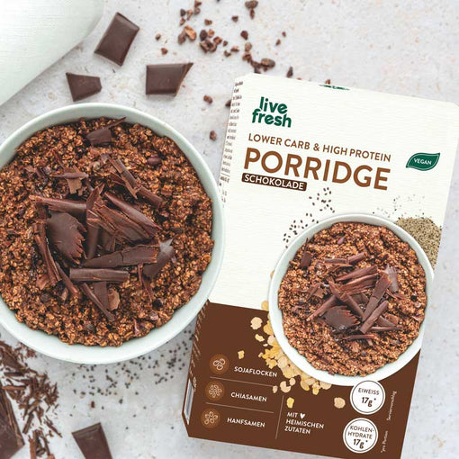 Schoko-Porridge: Eine Schüssel mit Schokoladen-Porridge, garniert mit dunklen Schokoladenraspeln. Um die Schüssel herum sind Schokoladenstücke und Kakaosplitter verteilt. Im Hintergrund die Verpackung von 