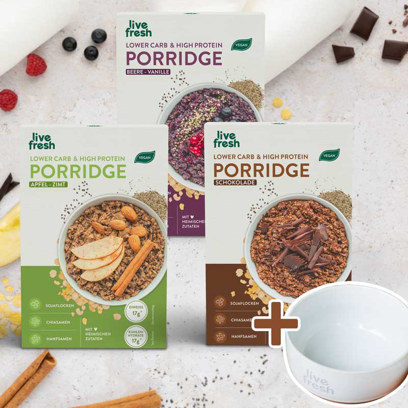 Porridge-Probierpaket mit Schüssel: Dasselbe Porridge-Probierpaket mit den drei Sorten, ergänzt durch eine weiße Keramikschüssel mit "Live Fresh"-Branding. Zutaten wie Zimtstangen, Beeren und Schokoladenstücke sind dekorativ um die Packungen verteilt.