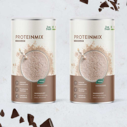 Zwei Dosen „Proteinmix Schokolade“ von LiveFresh mit cremigem Shake auf der Verpackung, umgeben von Schokoladenstücken. Der vegane Proteinshake enthält pflanzliches Eiweiß aus Soja, Erbse, Reis und Hanf und ist laktose- sowie glutenfrei.