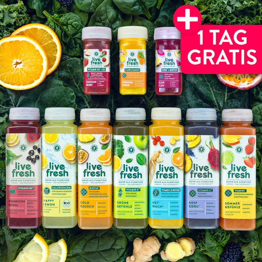 Verschiedene Flaschen und Shots einer Saftkur von LiveFresh stehen auf einem Bett aus grünem Blattgemüse, umgeben von Orangen, Zitrone, Ingwer, Brombeeren und Passionsfrucht. Die farbigen Säfte und Wellness Shots zeigen unterschiedliche Sorten für eine mehrtägige Saftkur. Werbegrafik mit dem Text "1 TAG GRATIS".